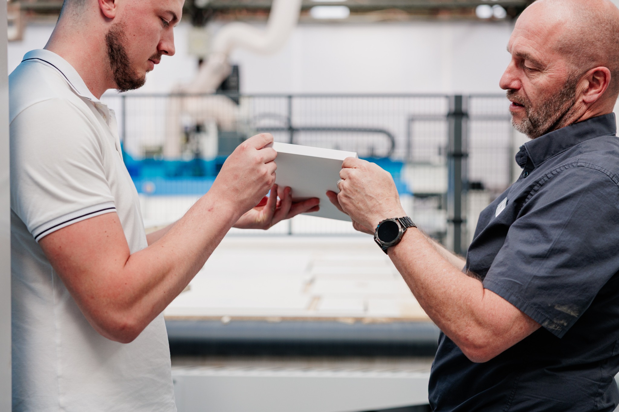 Twee mannen bekijken samen een bewerkt werkstuk naast een machine.